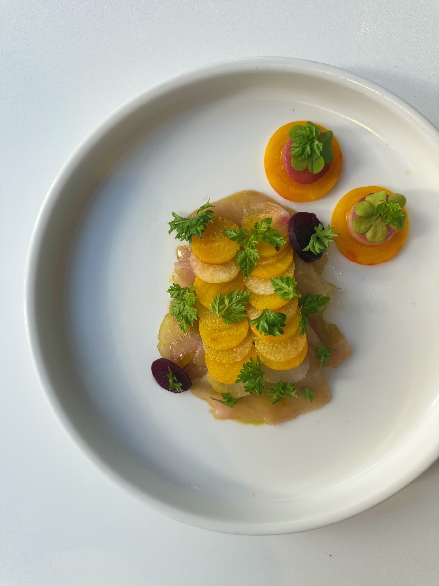 A composed plate with yellow vegetables and herbs